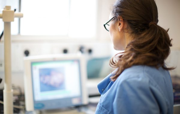 A woman in a blue uniform, looking at a computer screen in a laboratory