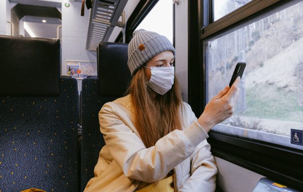 A young woman wearing a face mask and using a mobile phone on a train