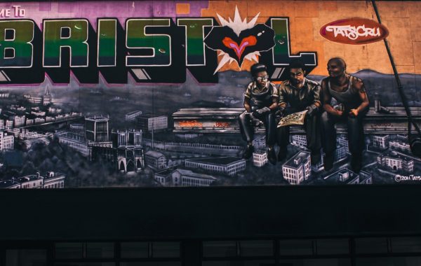 Street art showing the Bristol skyline with three young people sitting in front of it