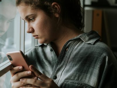 A young person with a mobile phone looks out of a window