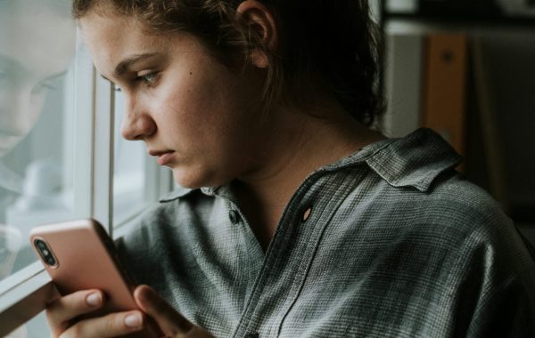 A young person with a mobile phone looks out of a window