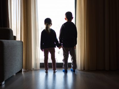 Two children from behind holding hands and looking out of a window