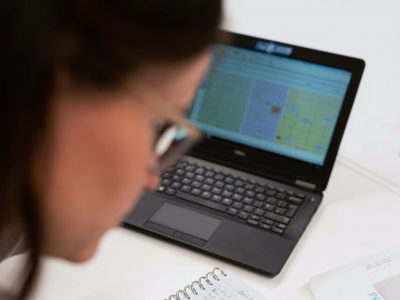 Woman sitting at her desk writing notes whilst looking at data on her laptop
