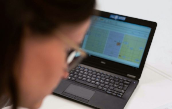 Woman sitting at her desk writing notes whilst looking at data on her laptop