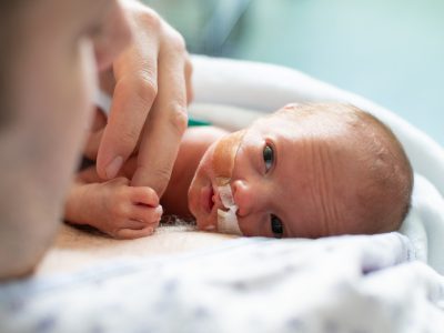 A father holds hands with his premature baby in hospital