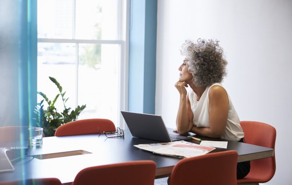 A woman looks reflectively out of a window while sitting at a computer
