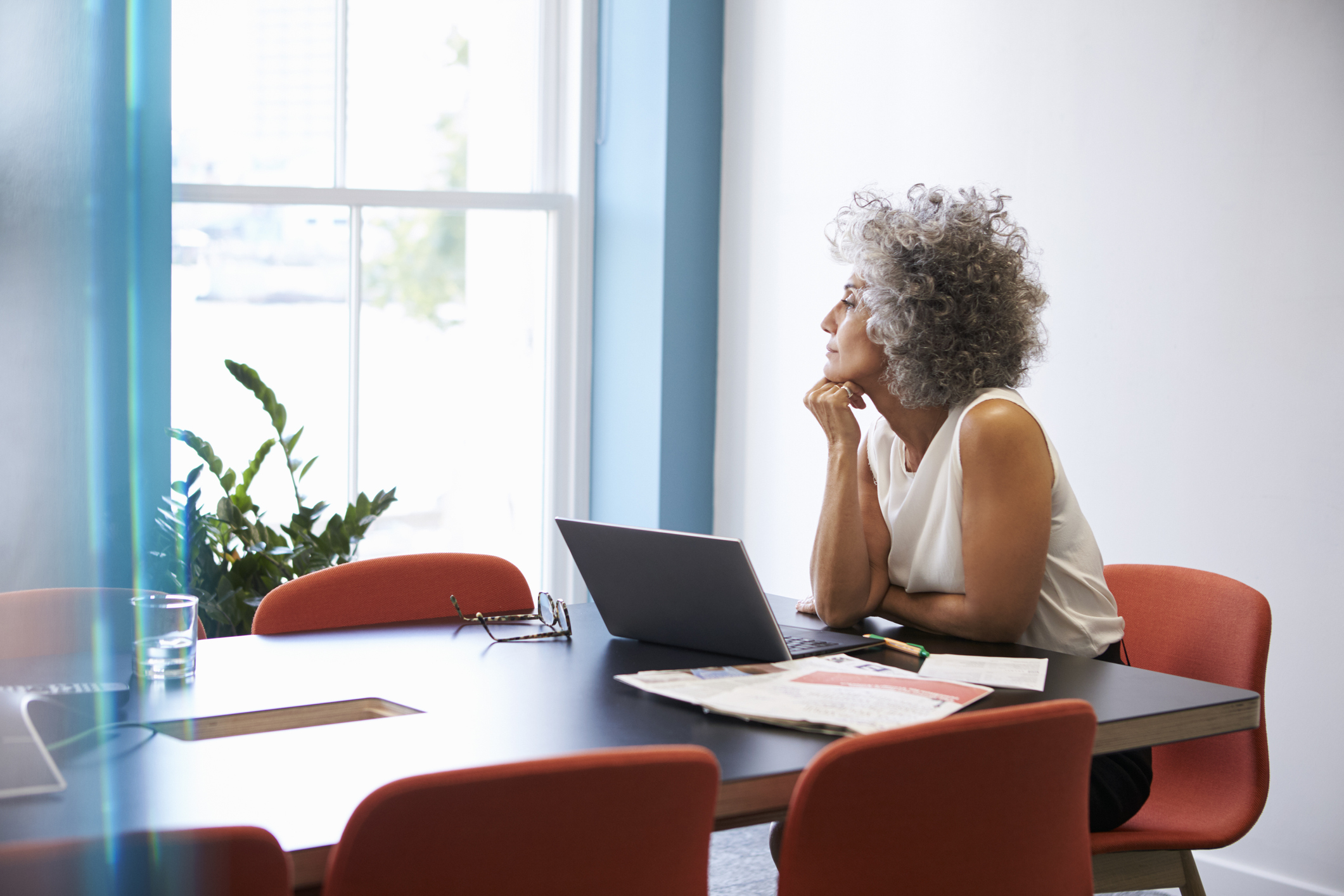 A woman looks reflectively out of a window while sitting at a computer
