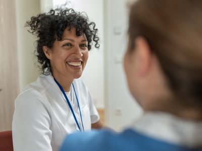 A smiling woman wearing a lanyard talking to another person