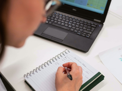 A scientist working at a computer and writing on a pad