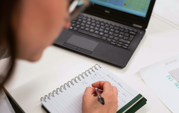 A scientist working at a computer and writing on a pad