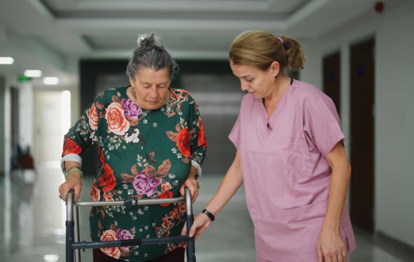 A nurse is assisting a senior adult patient walking down a hospital corridor
