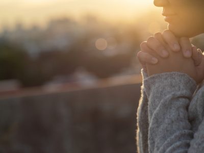 A woman clasps her hands in hope with the sunrise behind her