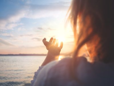 A woman at sunrise over the sea, cupping the sun in her hands