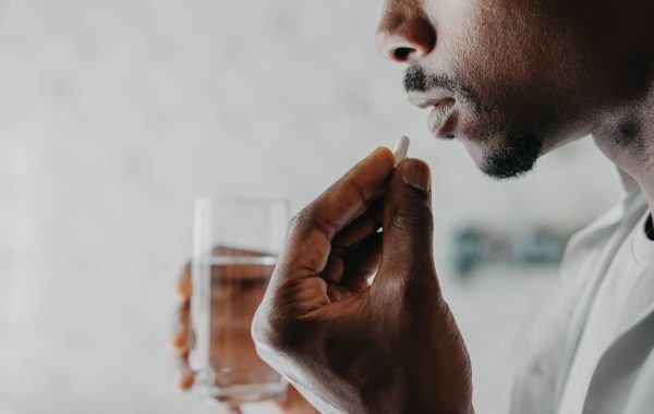 A man is holding a glass of water about to take a sip with his medication