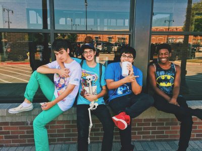 Four ethnically diverse young men are sitting on a low wall with their backs against a restaurant window