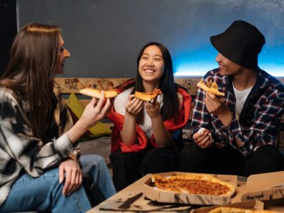 A group of teenagers are sitting around talking and sharing a pizza