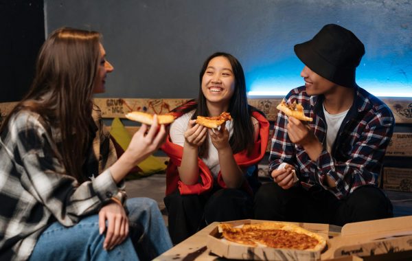 A group of teenagers are sitting around talking and sharing a pizza