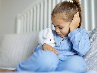 Girl on a sofa hugging a teddy and clutching her ear