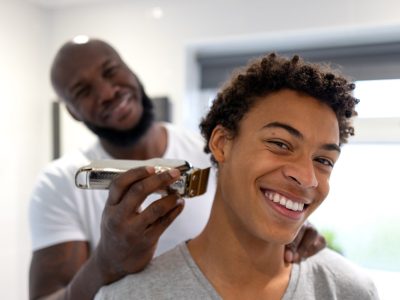 A young Black man gets his hair cut by a barber