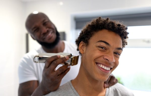 A young Black man gets his hair cut by a barber